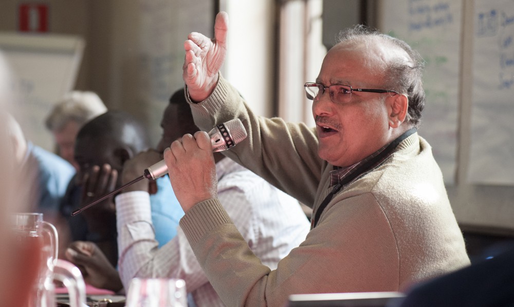 Dr. Upadhyaya with his hand in the air as he speaks at a meeting. 