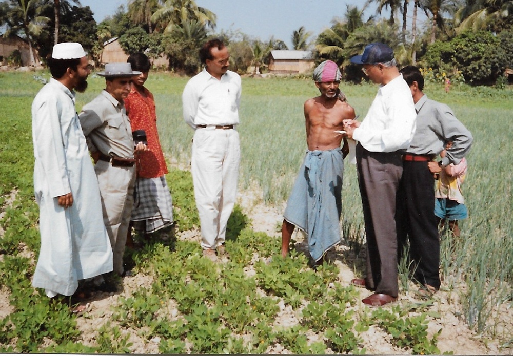 Seven men standing in field observing crops.